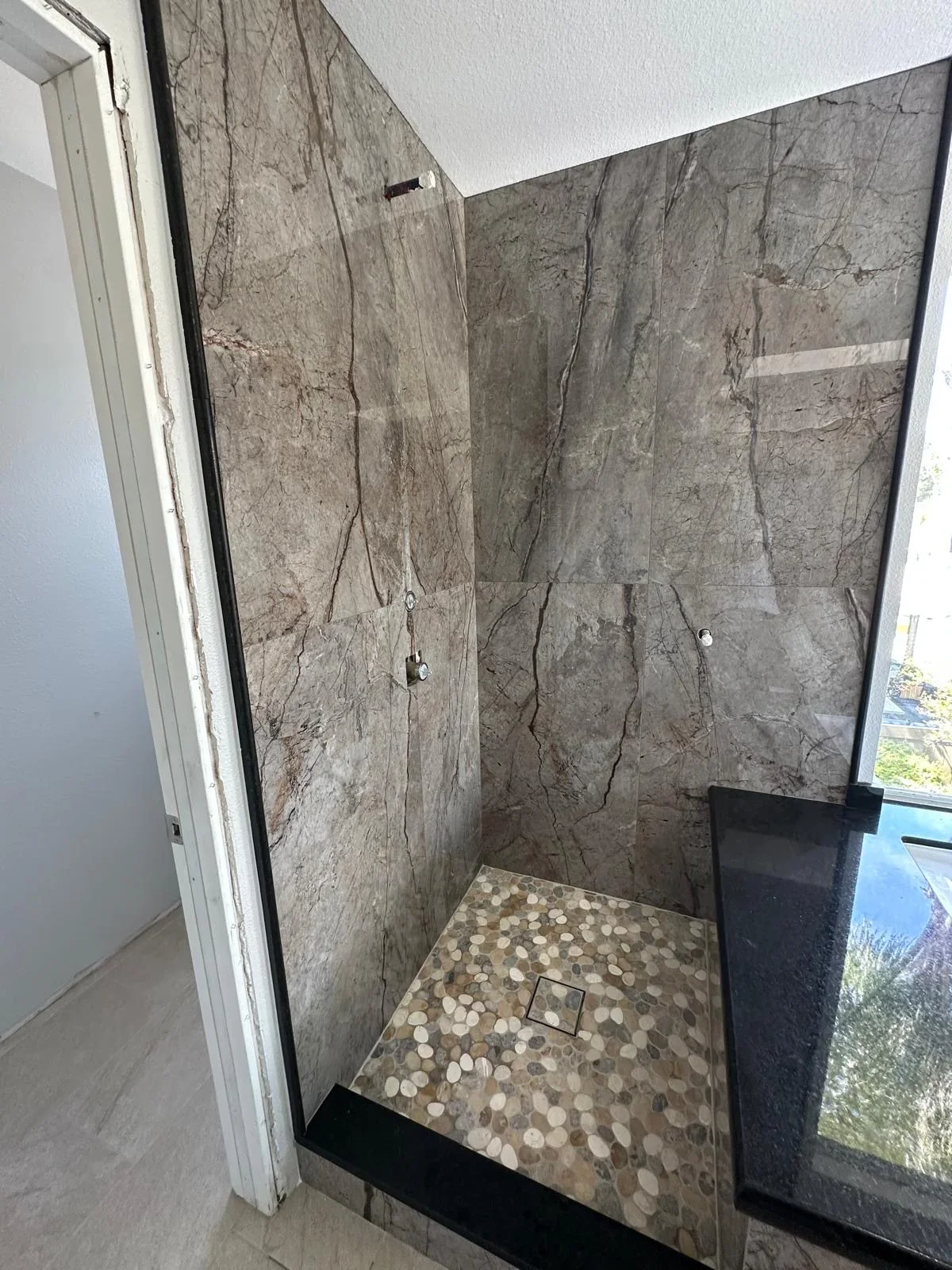 Gray marble tile shower walls with penny tile mosaic floor and black trim