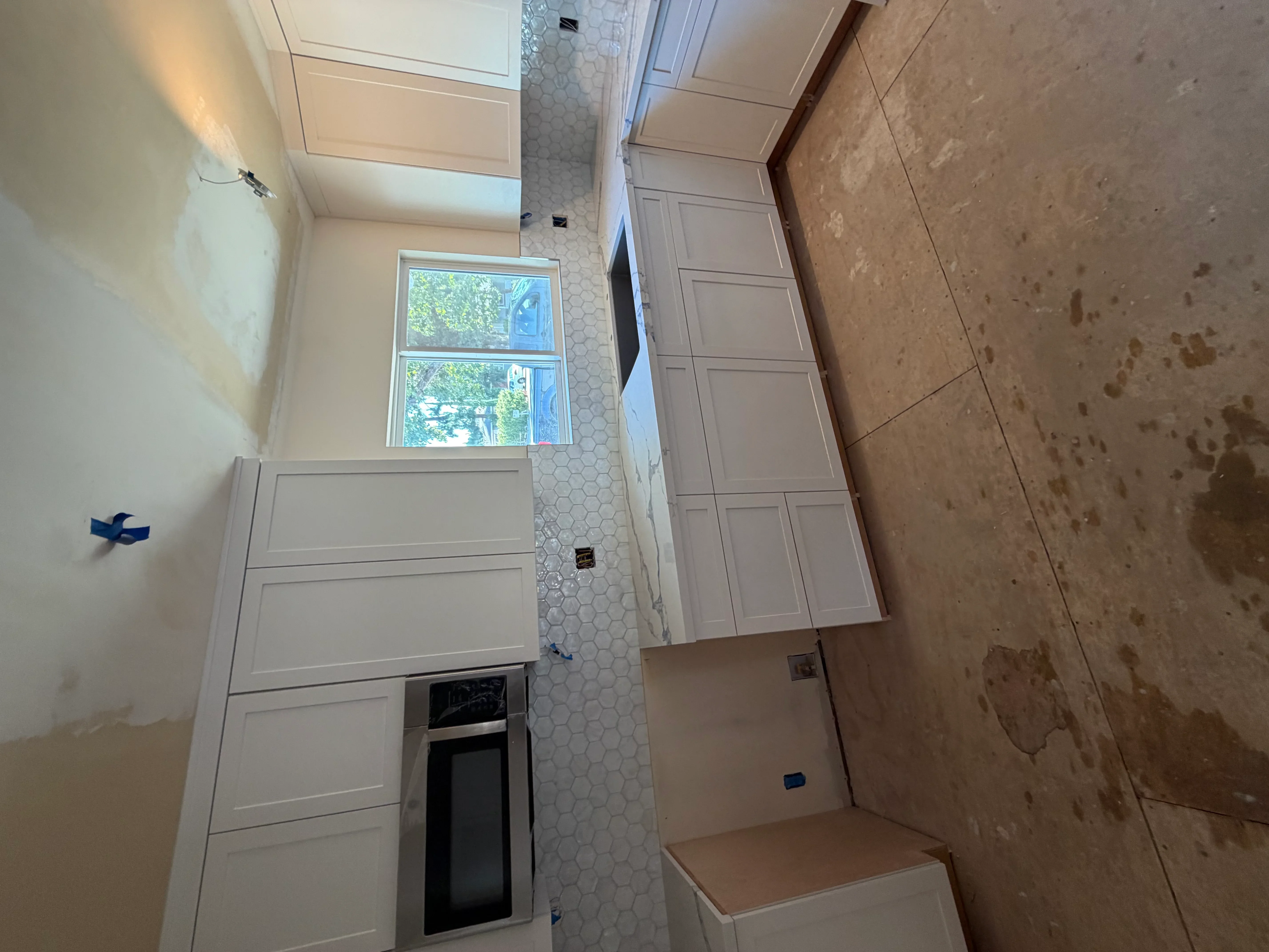 Bathroom under renovation with hexagonal tile shower surround and white cabinetry