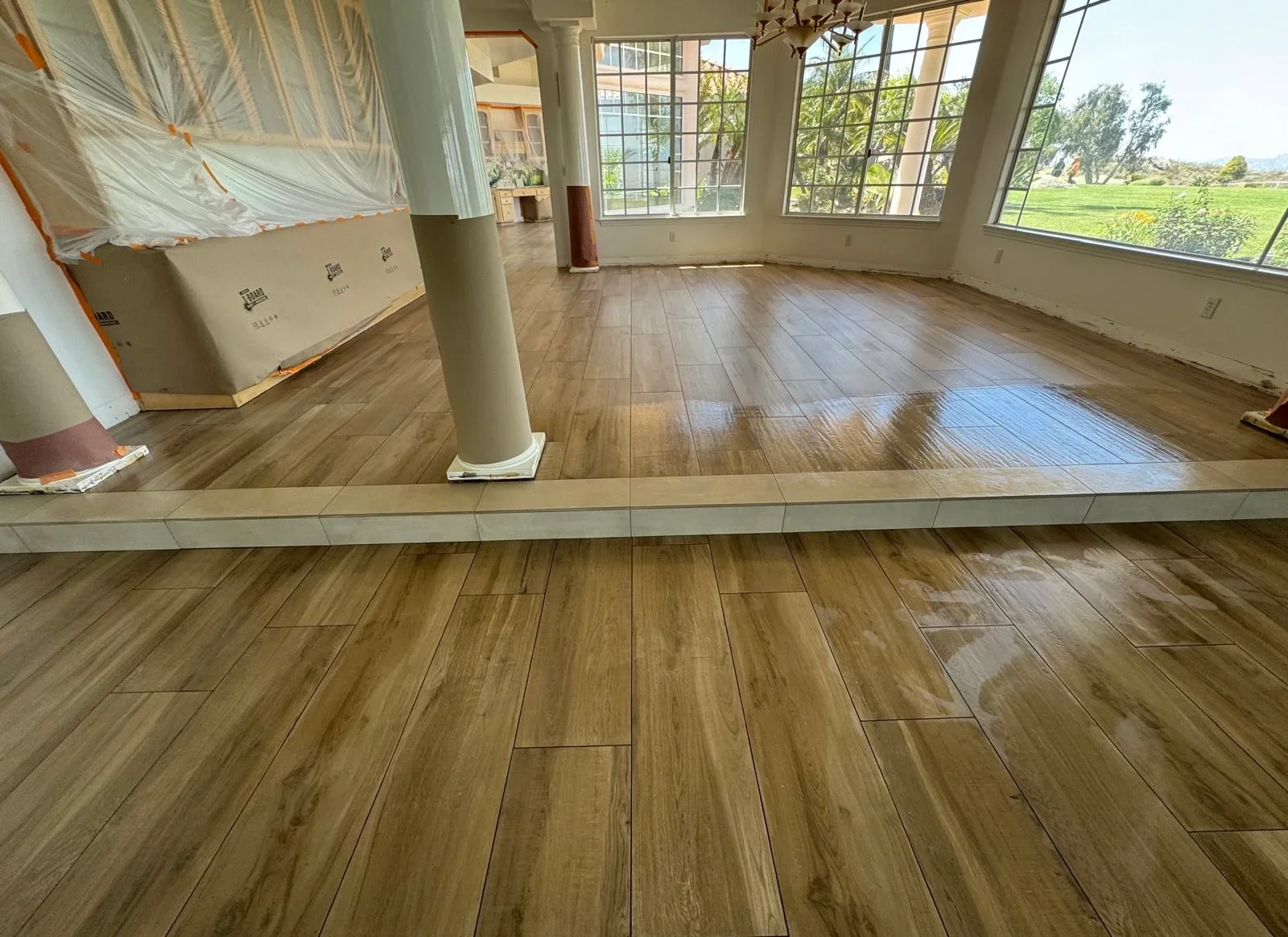 Wood-look tile flooring installation in bright open room with large windows overlooking fields