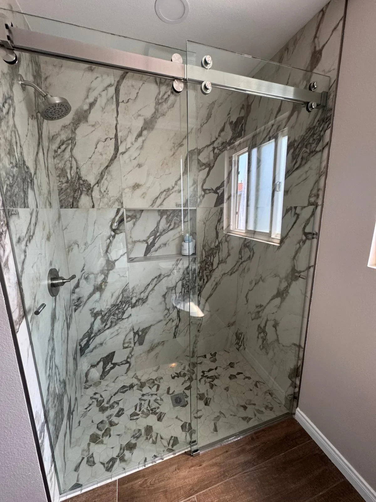 Marble tile shower with frameless glass sliding doors and chrome fixtures