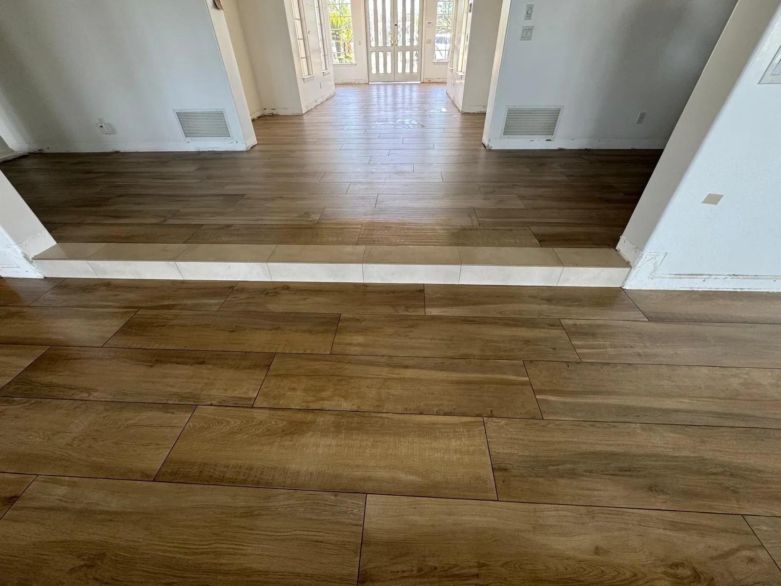 Wood-look tile flooring in entryway with white trim and glass doors