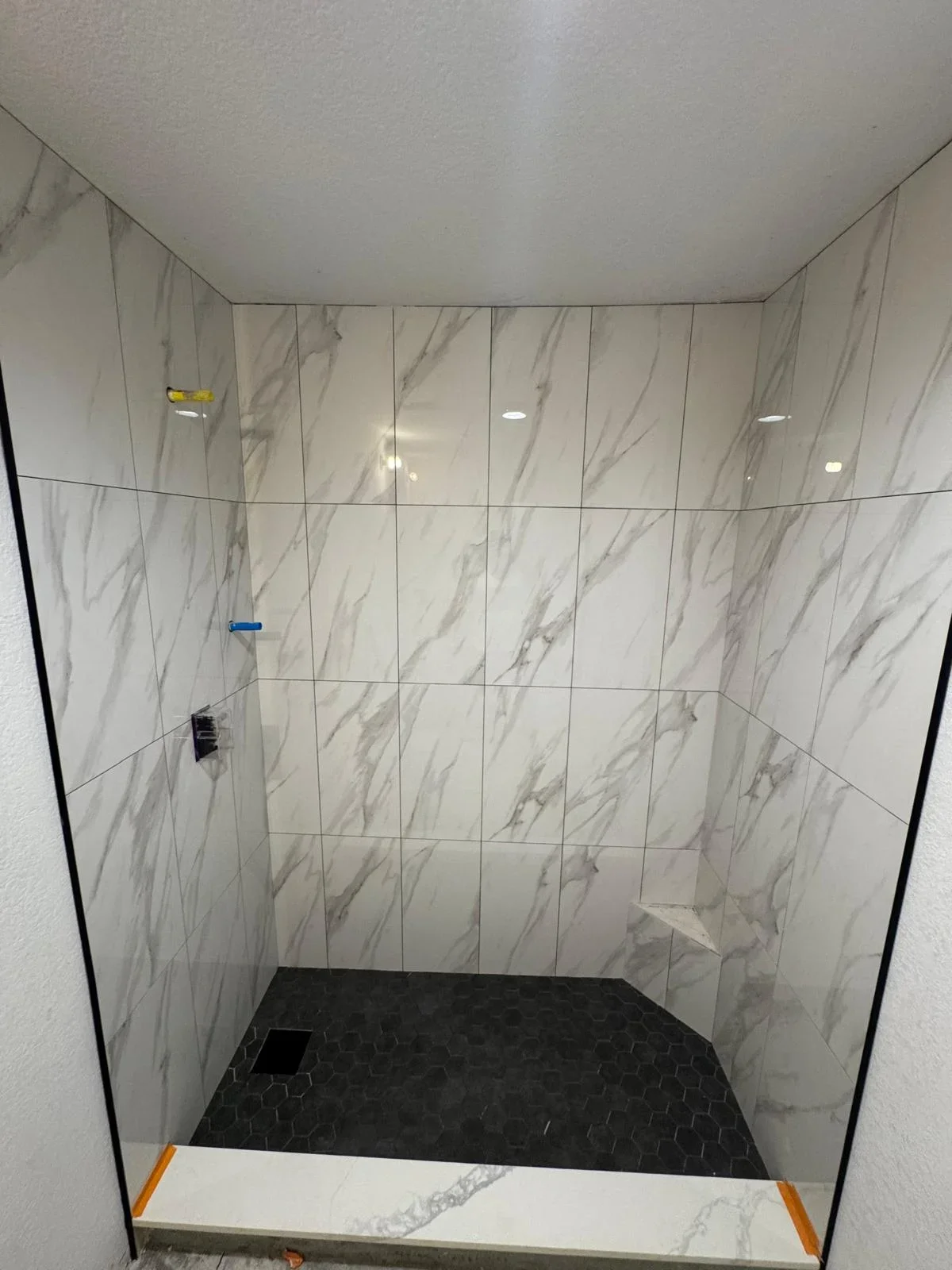 Marble-look tile shower with black hexagonal floor and recessed lighting