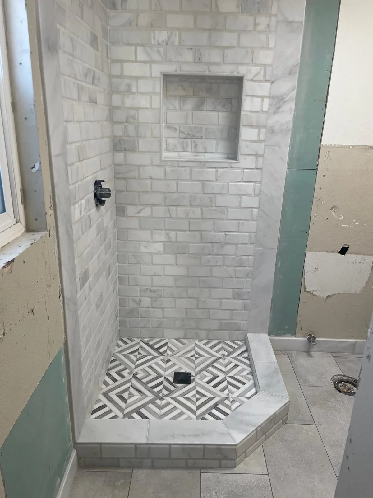 Modern shower enclosure with white marble subway tiles and geometric patterned floor