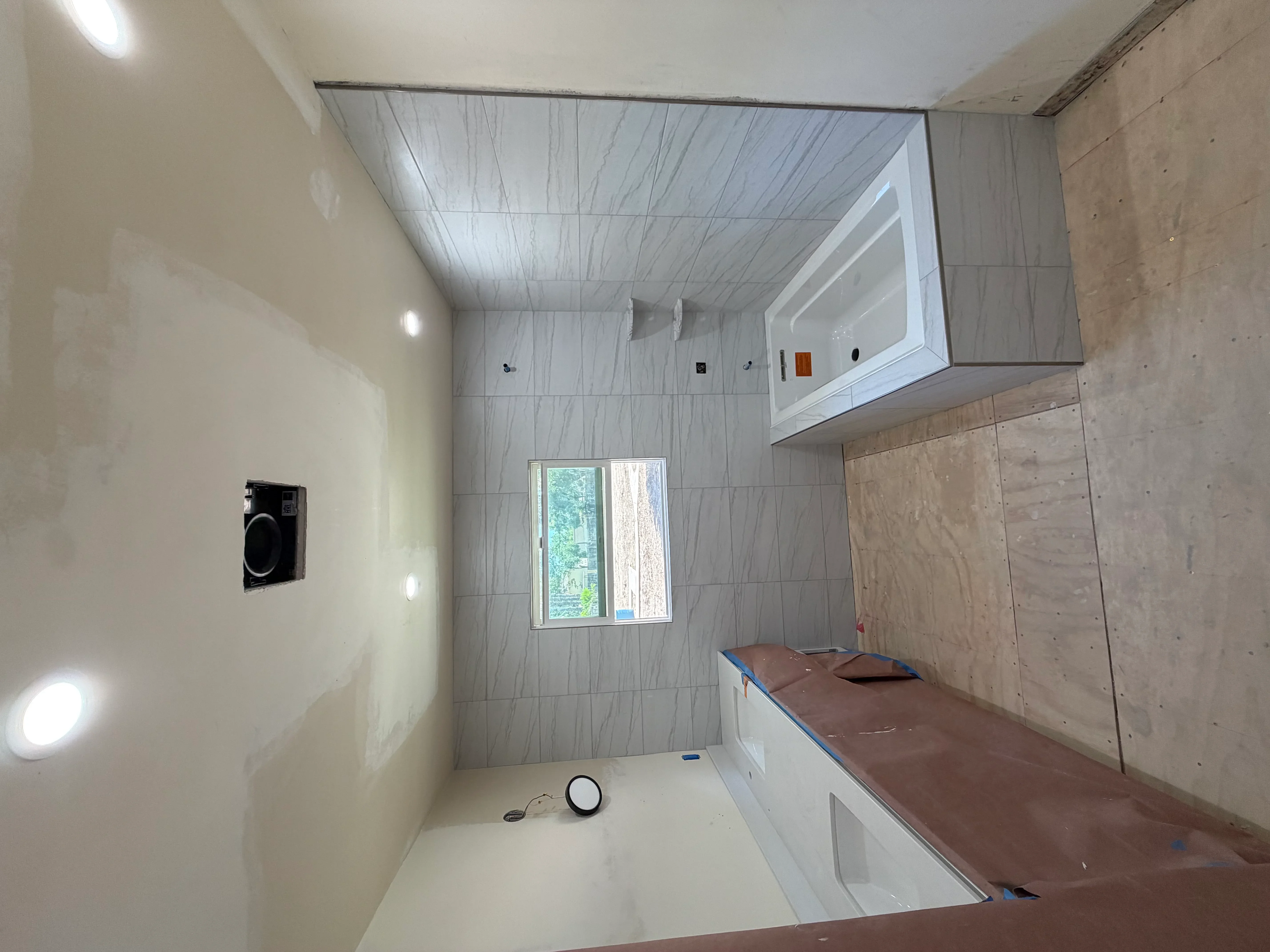 Bathroom under renovation with gray marble tile walls, white mirror cabinet, and recessed lighting