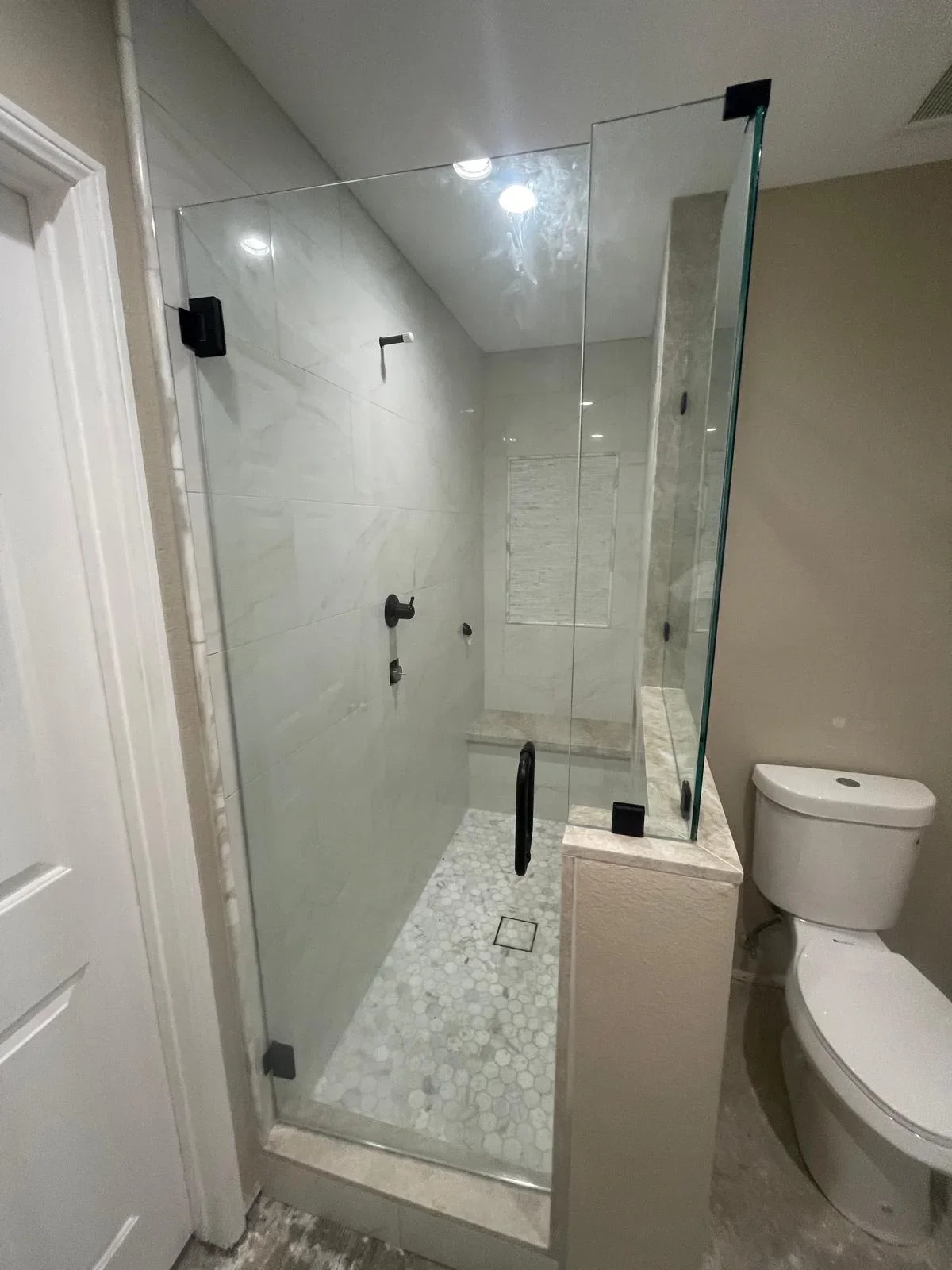 Modern bathroom shower with white marble tile walls, hexagon floor mosaic, and frameless glass door