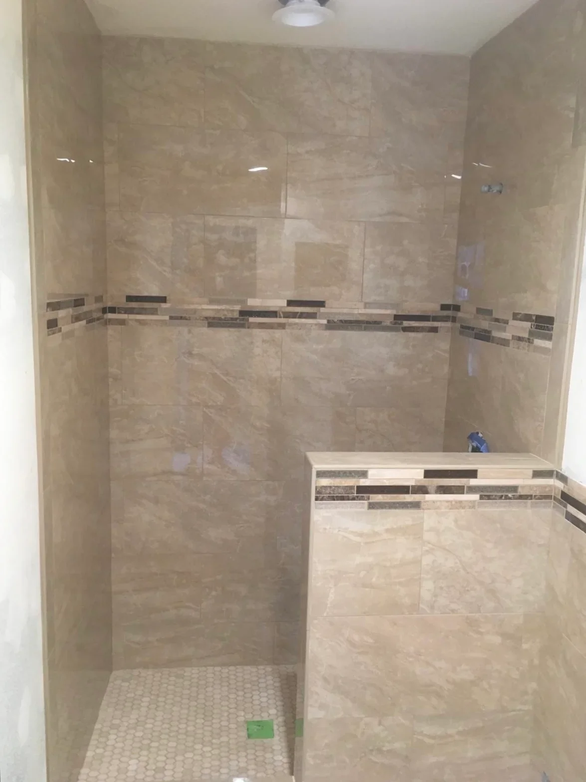 Modern travertine shower with glass doors, built-in bench, and decorative tile accents