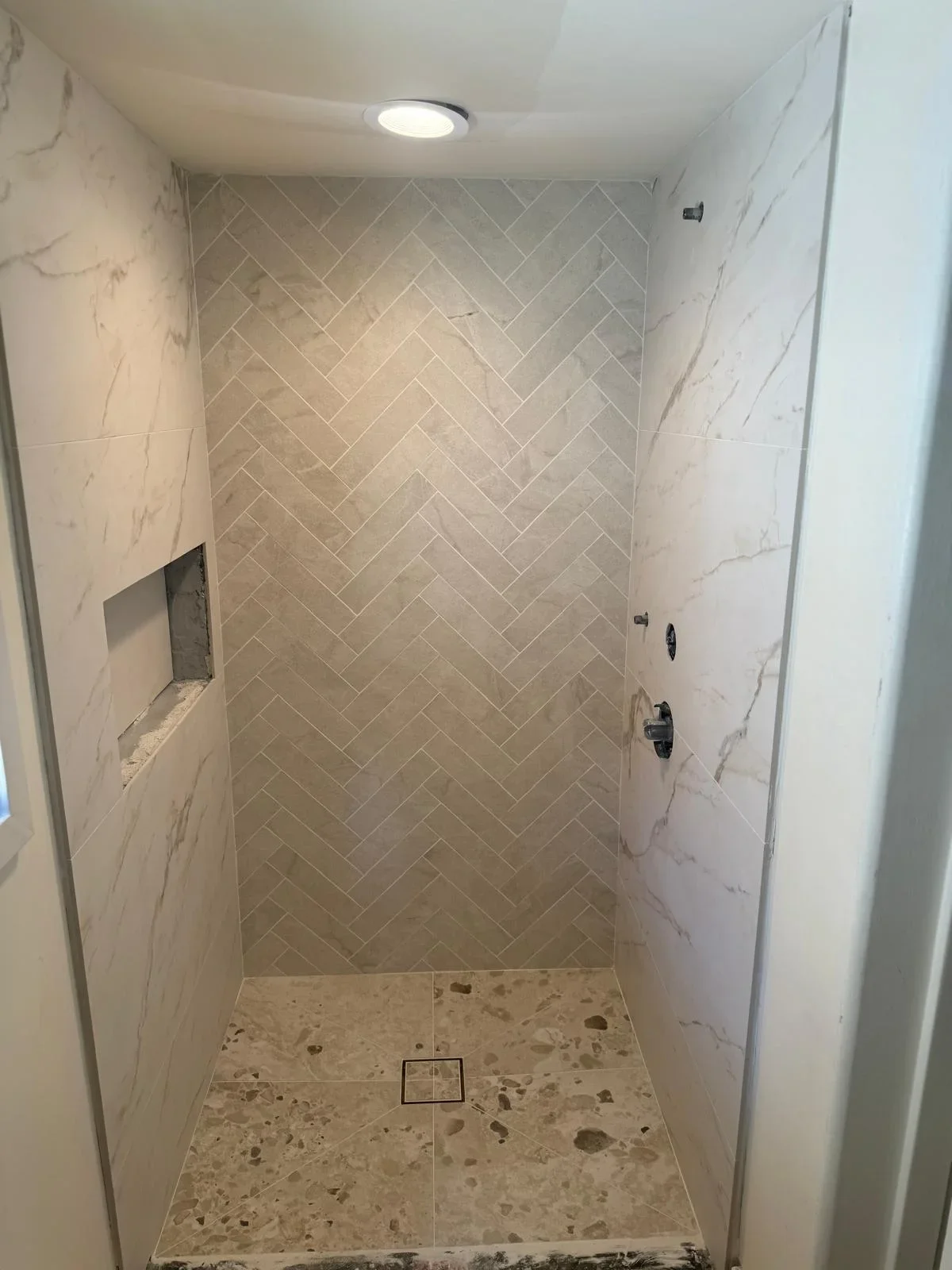 Marble herringbone tile shower with terrazzo floor and recessed lighting in Fullerton