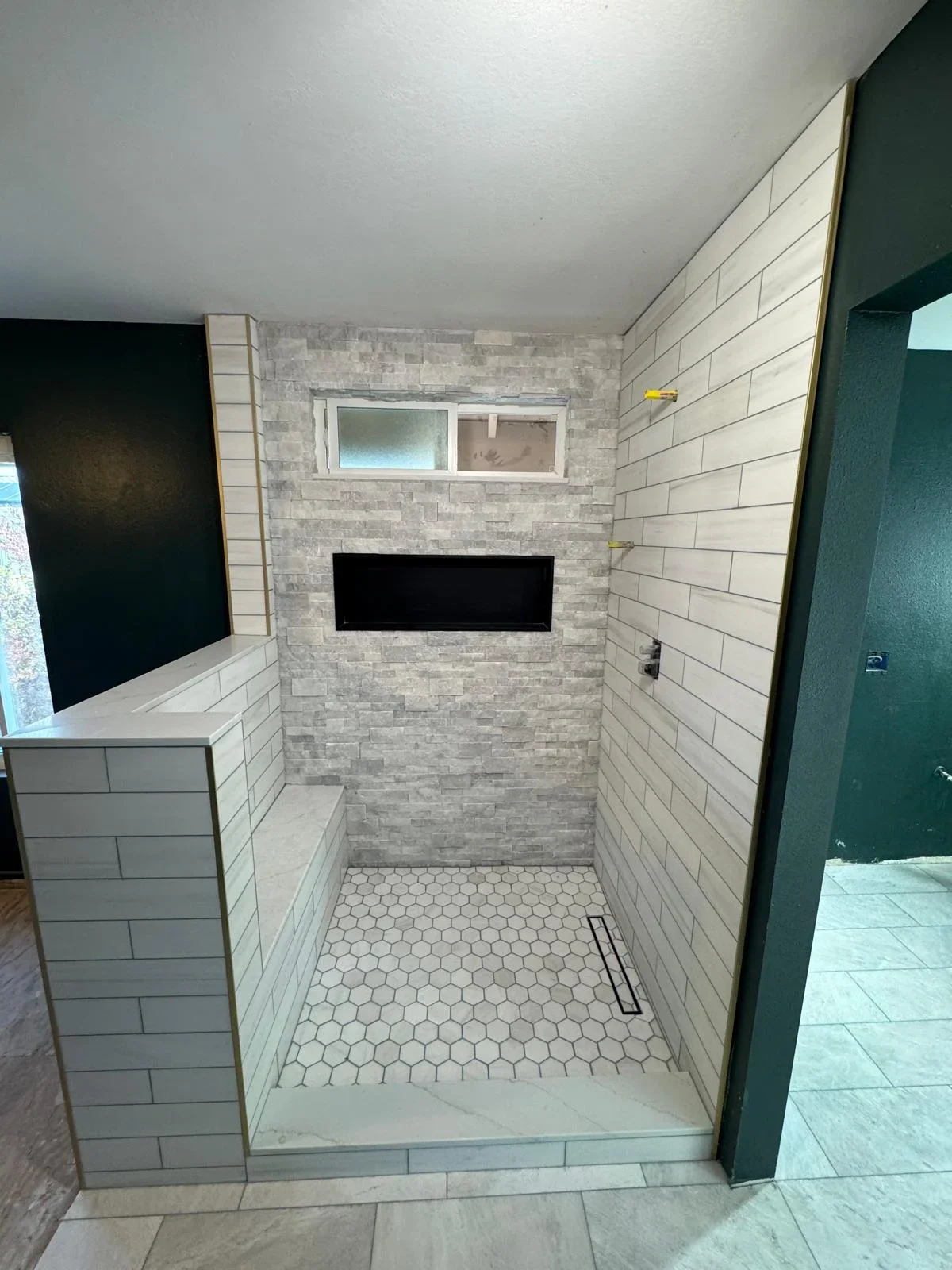 Modern bathroom shower with white subway tile, stone accent wall, and hexagonal floor tile