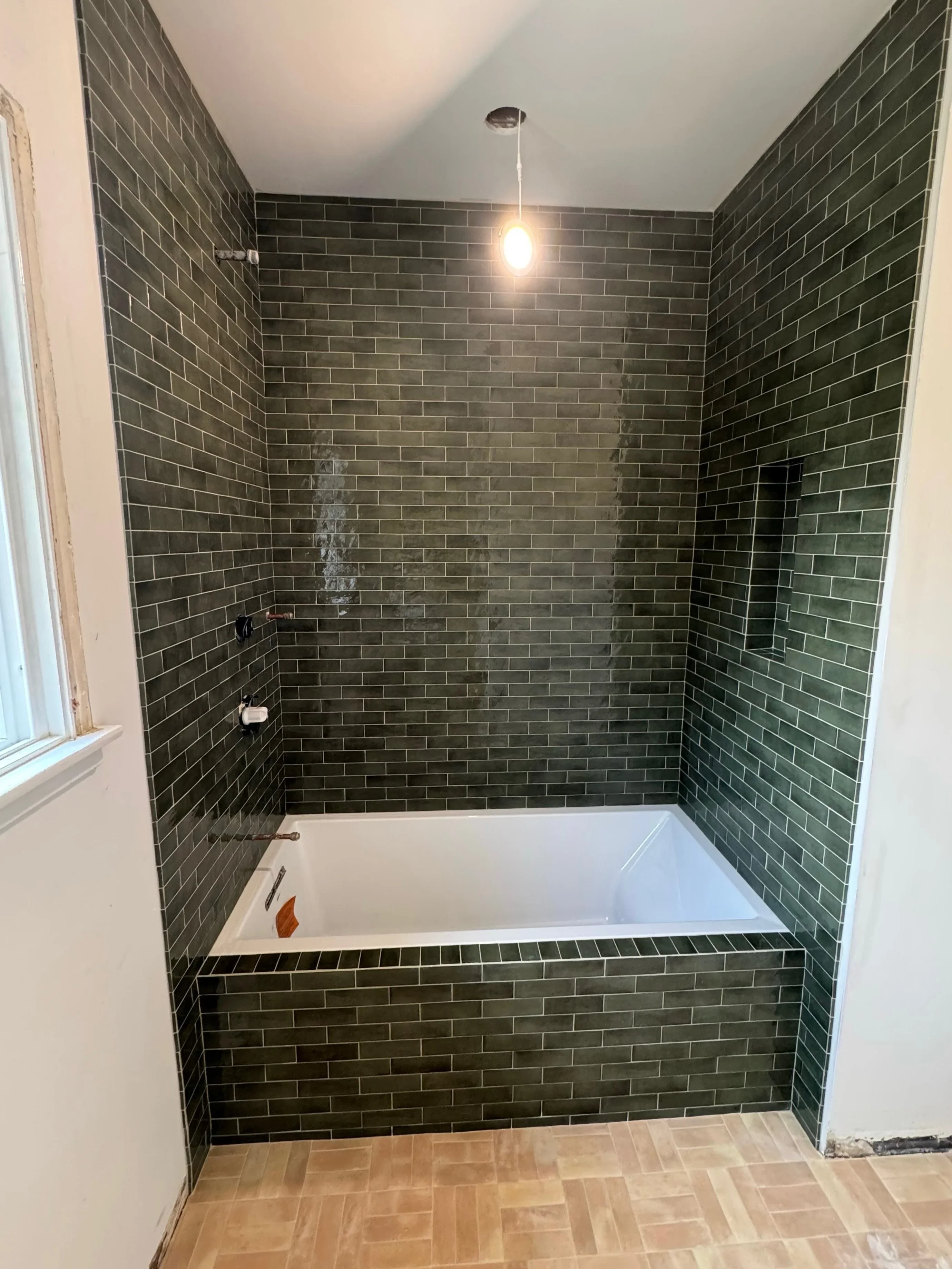 Dark green subway tile bathroom with white soaking tub and pendant light fixture