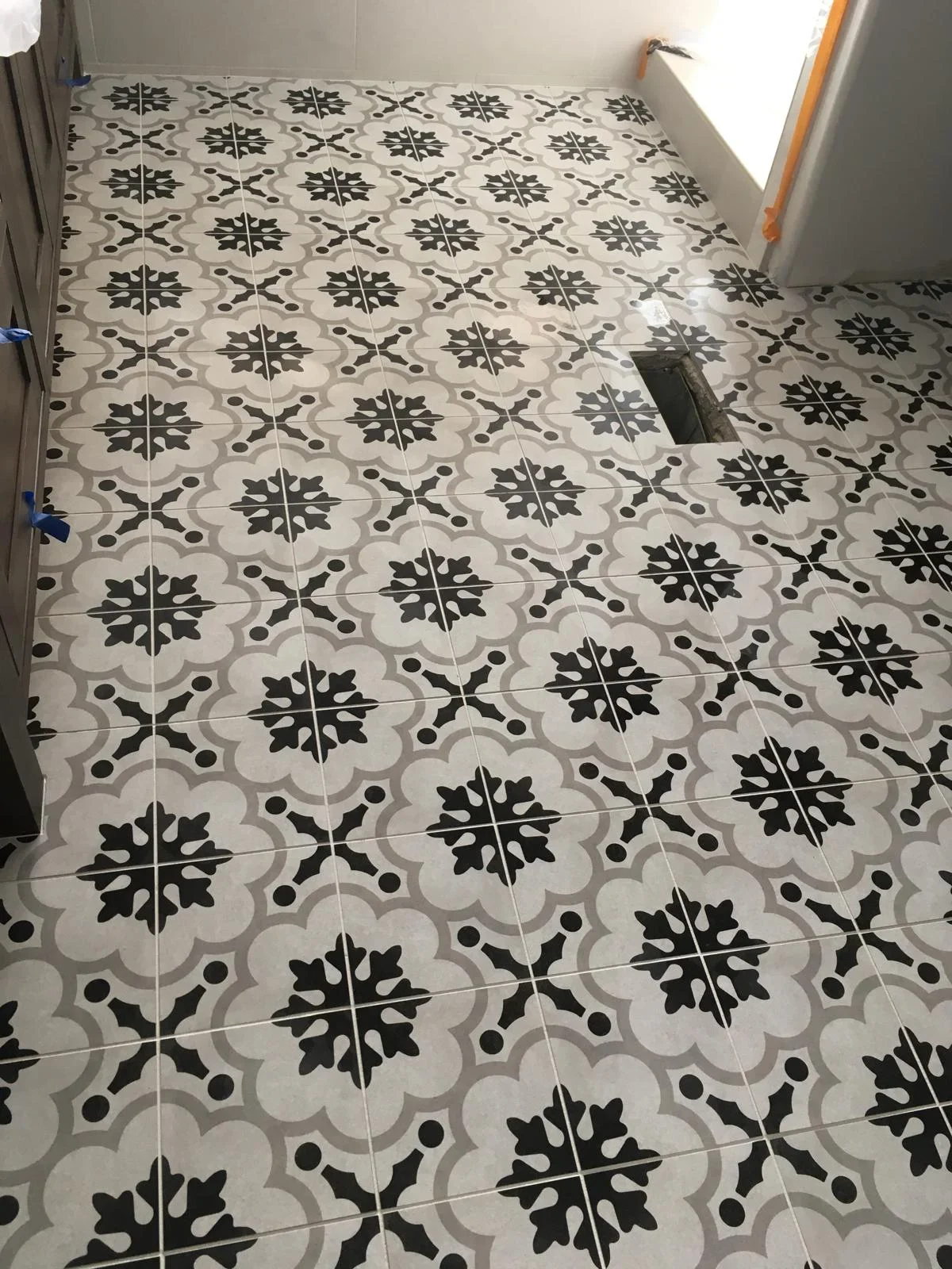 Black and gray patterned ceramic floor tiles with geometric floral design installed in grid layout