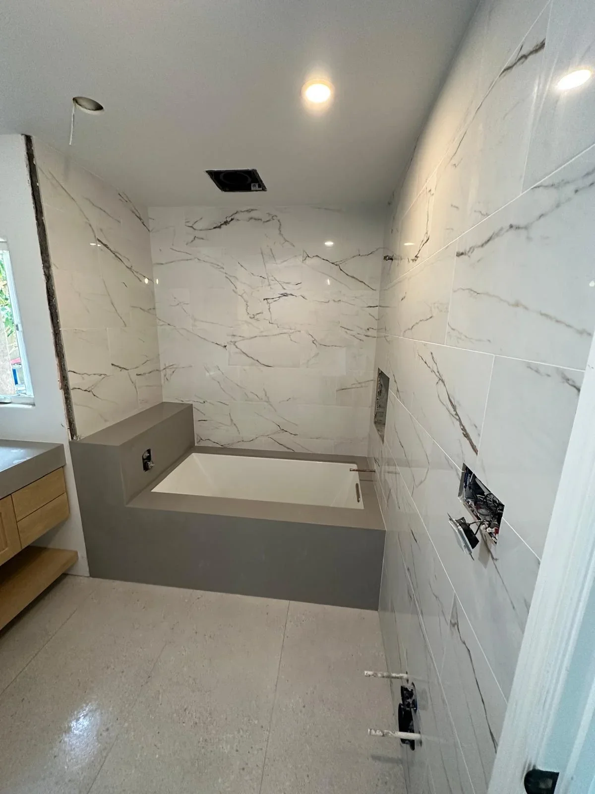 Modern bathroom with marble tile walls, gray soaking tub, and recessed lighting