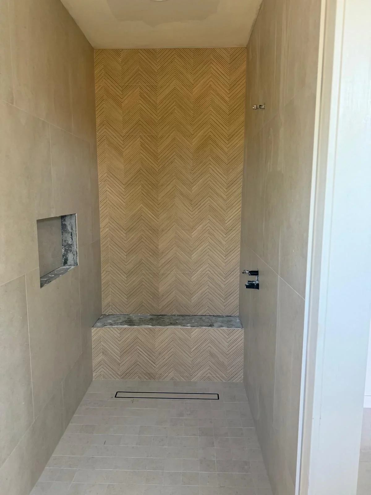 Modern shower with herringbone tile pattern on back wall and built-in bench