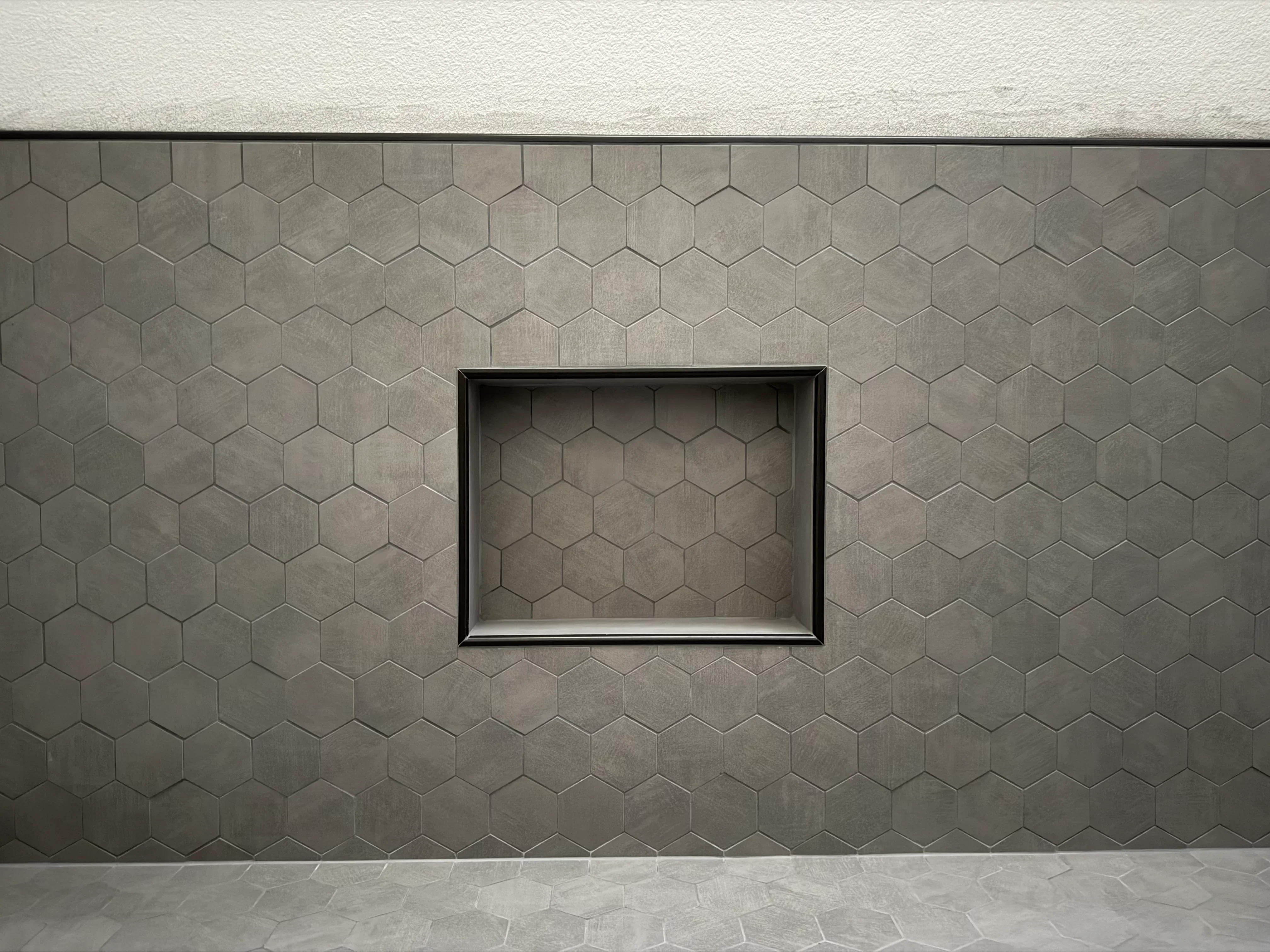 Gray hexagonal tiles with recessed metal-framed niche in center of wall