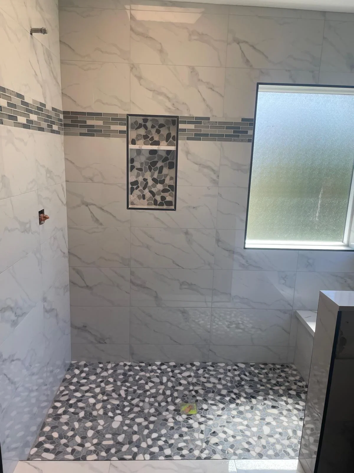 Modern shower with marble walls, pebble mosaic floor, and glass tile accent strip