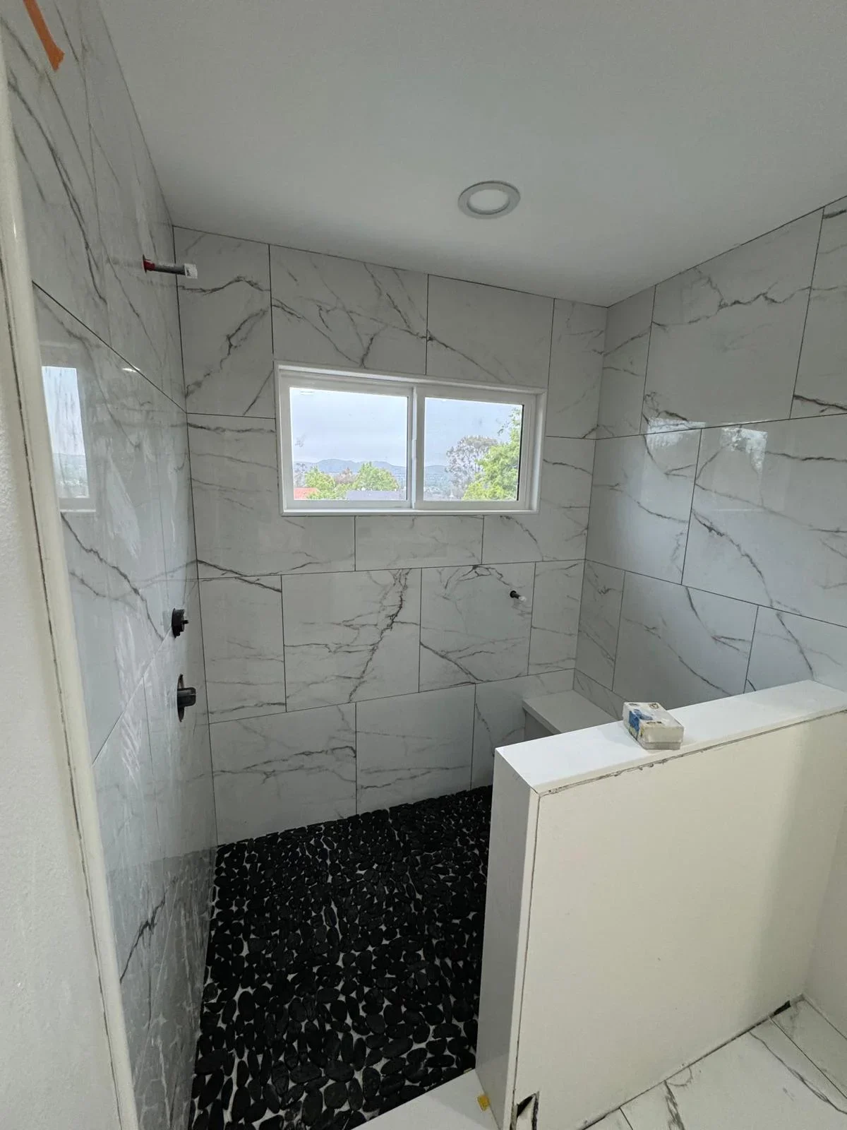 Modern bathroom with marble-look tile shower, black speckled floor, and frameless glass door