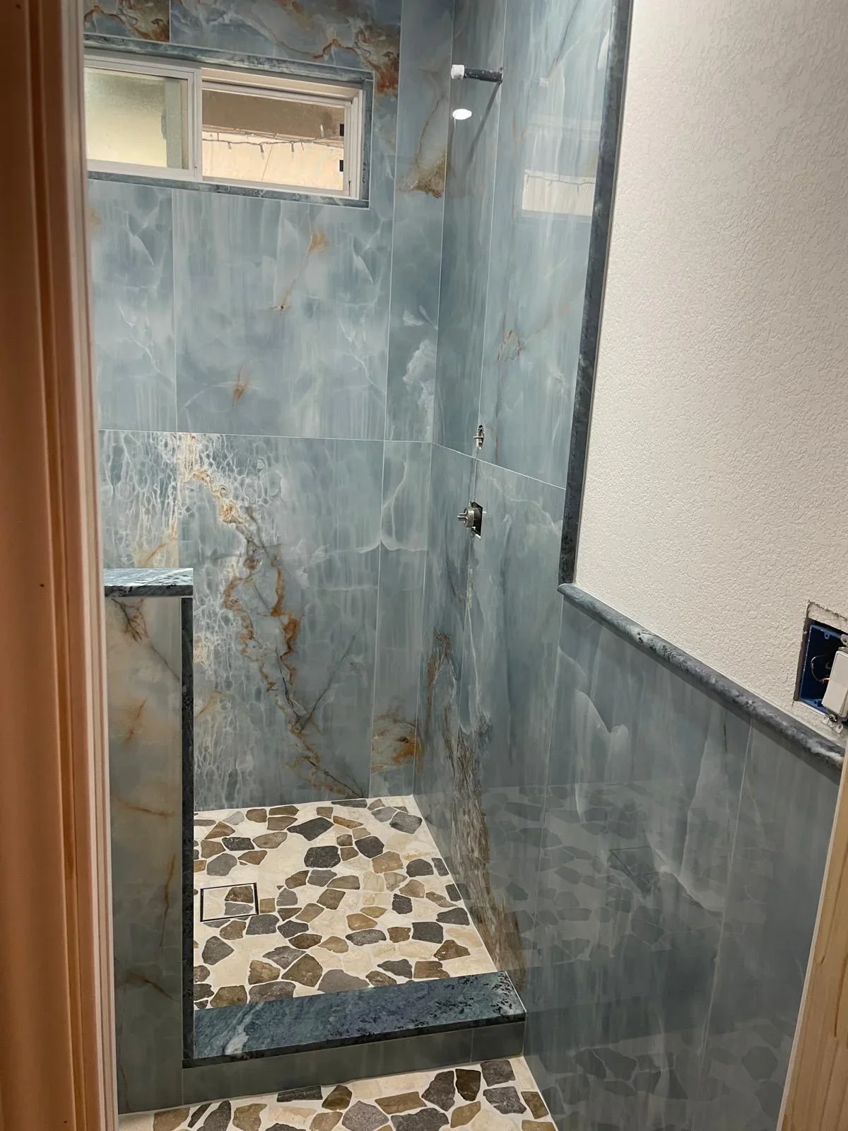 Modern bathroom shower with gray marble-look tile walls and river rock mosaic floor