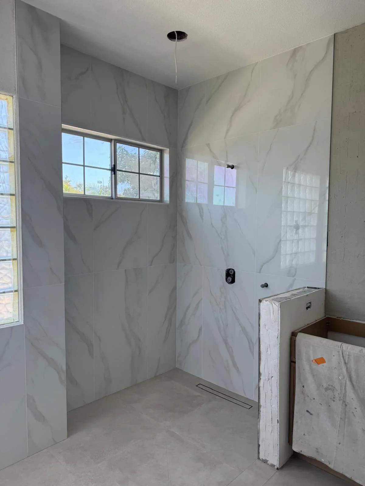 Modern bathroom shower with marble-look tile walls, glass enclosure, and linear drain