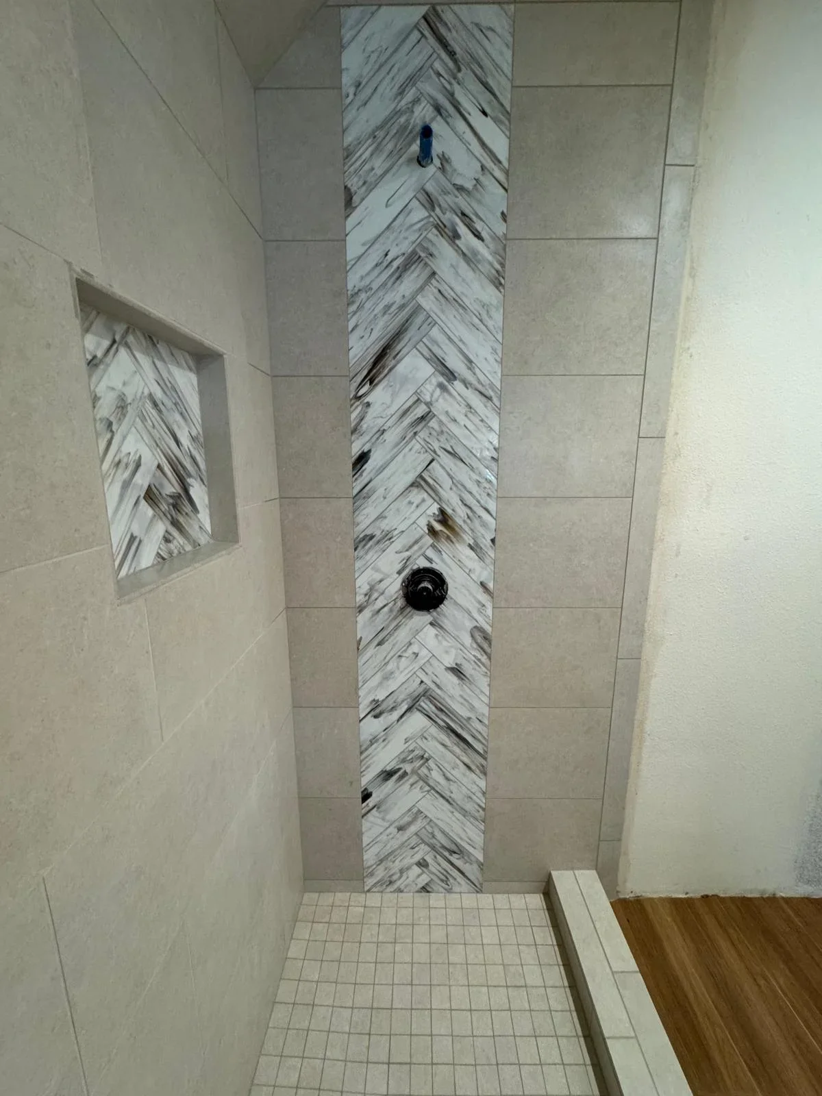 Herringbone marble tile accent wall in modern shower with recessed niche and neutral surround tiles