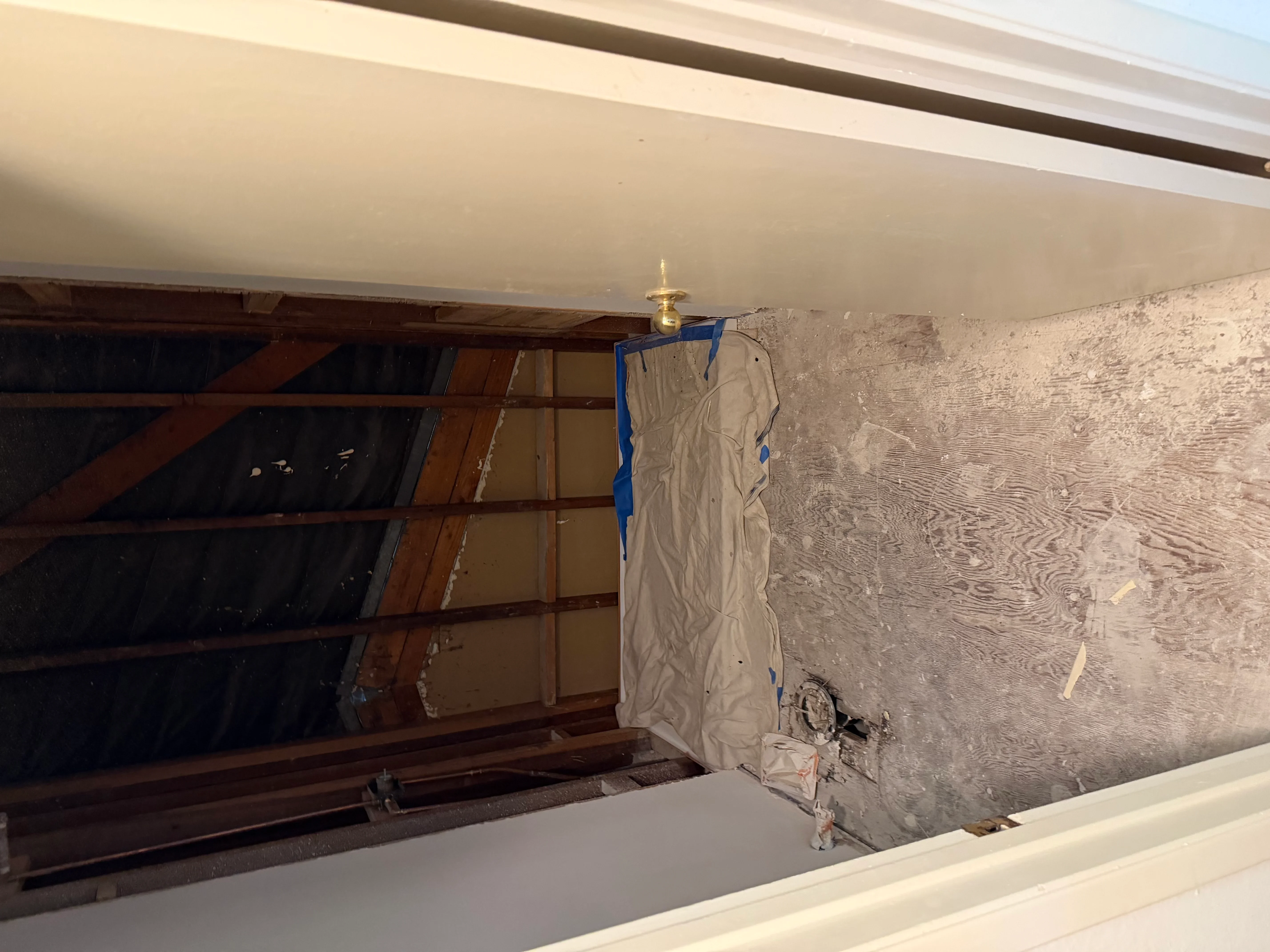 New drywall ceiling installation in garage with wooden framing and brass light fixture