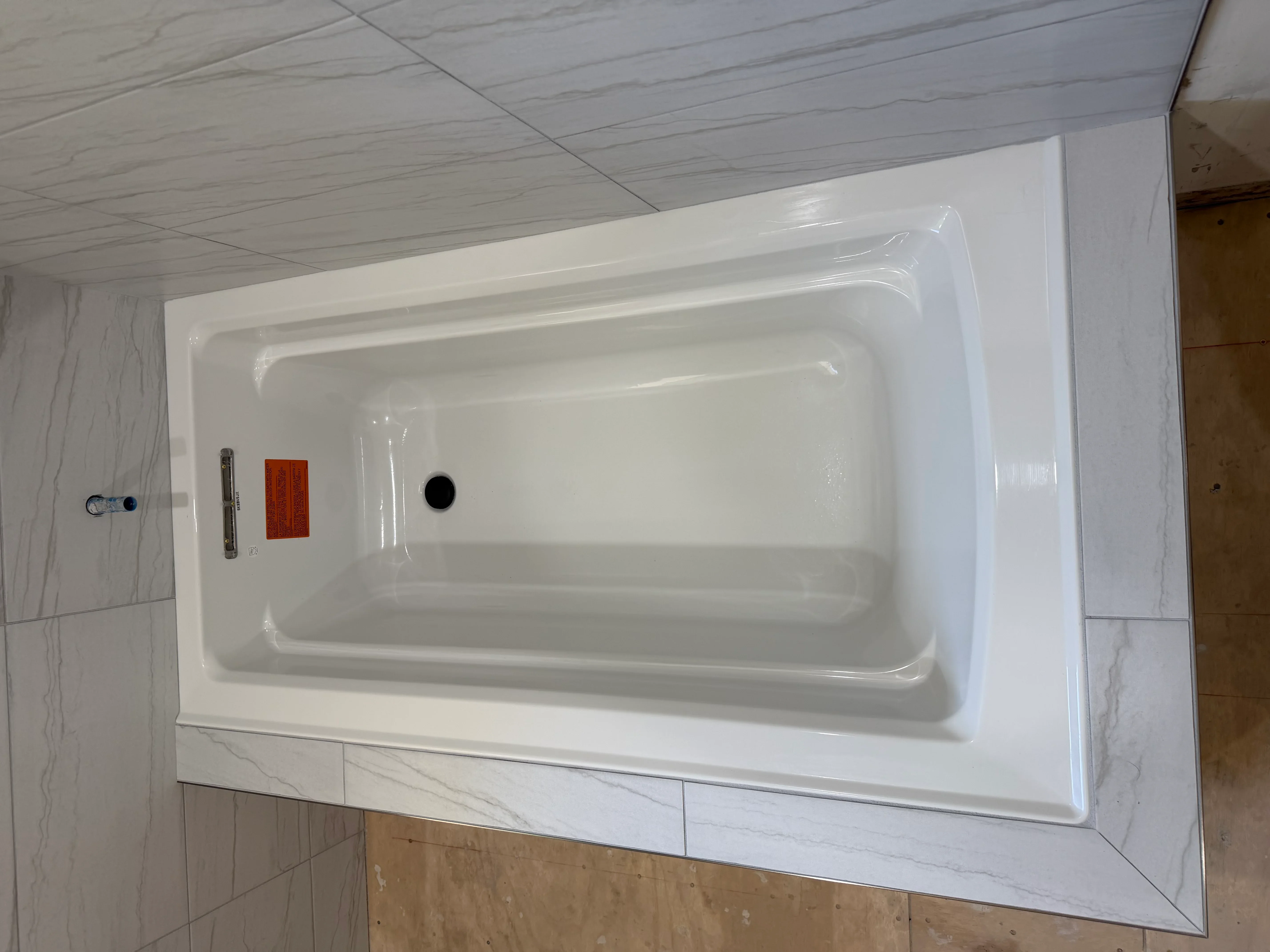 White bathtub with marble-look tile surround in modern bathroom installation