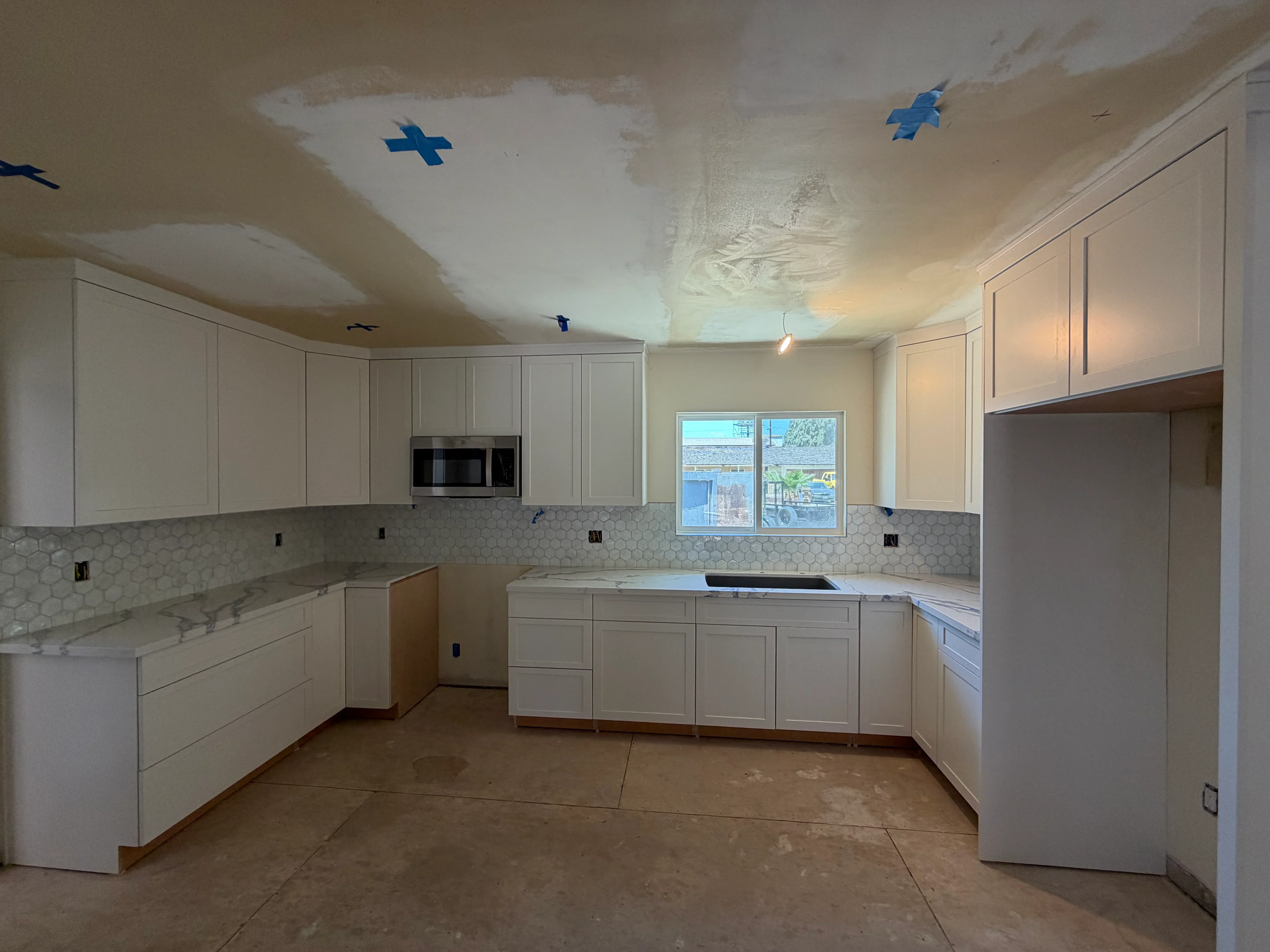 White kitchen with hexagonal tile backsplash, marble counters, and built-in appliances