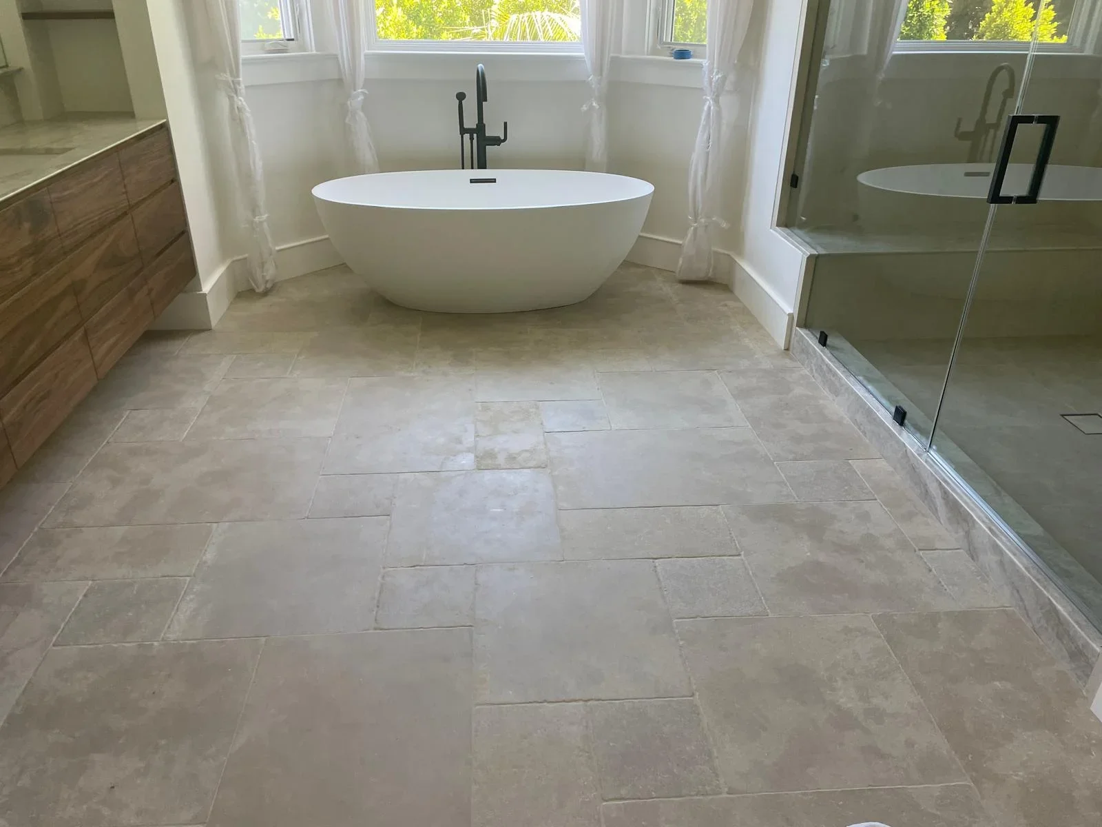 Modern bathroom with white soaking tub, travertine tile floor, and glass shower