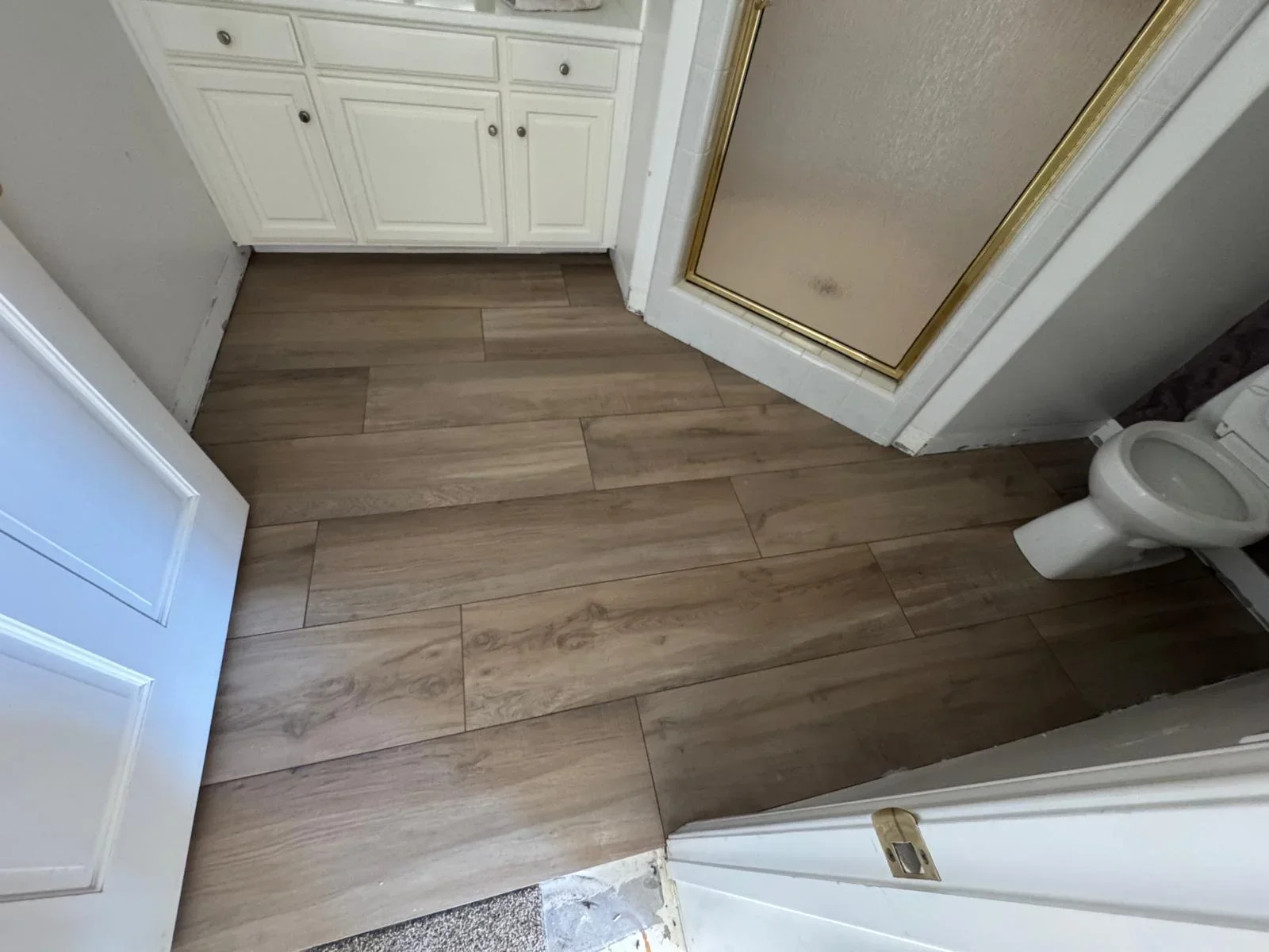 Bathroom with herringbone wood-look tile flooring, white vanity, and toilet installation