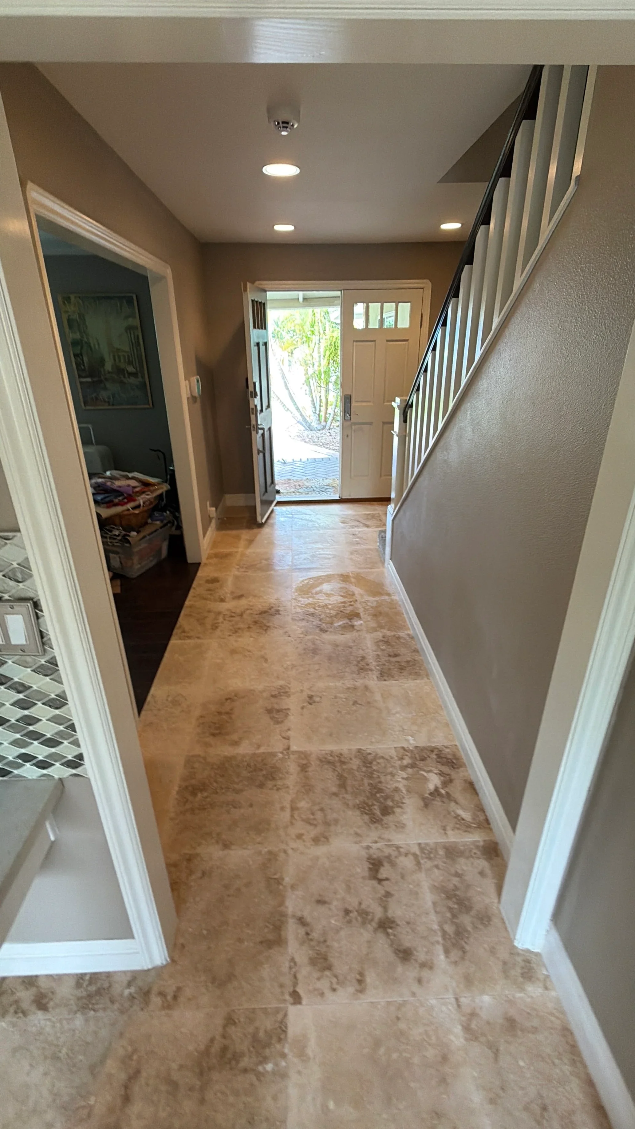 Travertine tile entryway with staircase, white trim, and recessed lighting
