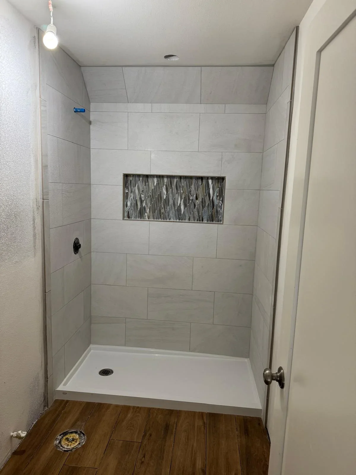 Modern bathroom shower with gray subway tile walls and textured accent niche