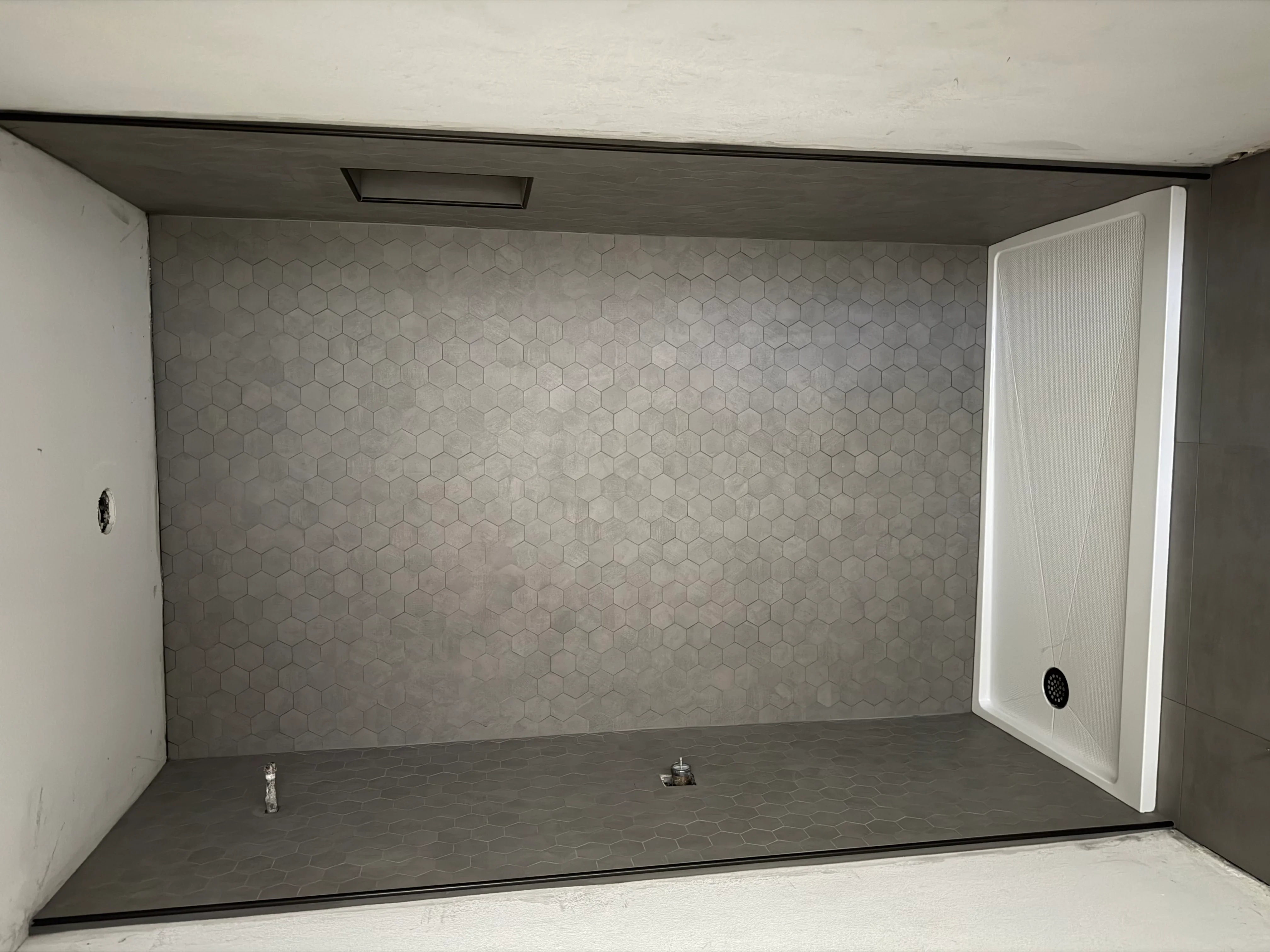 Newly installed shower with hexagonal tile walls and floor, white glass door, and recessed lighting