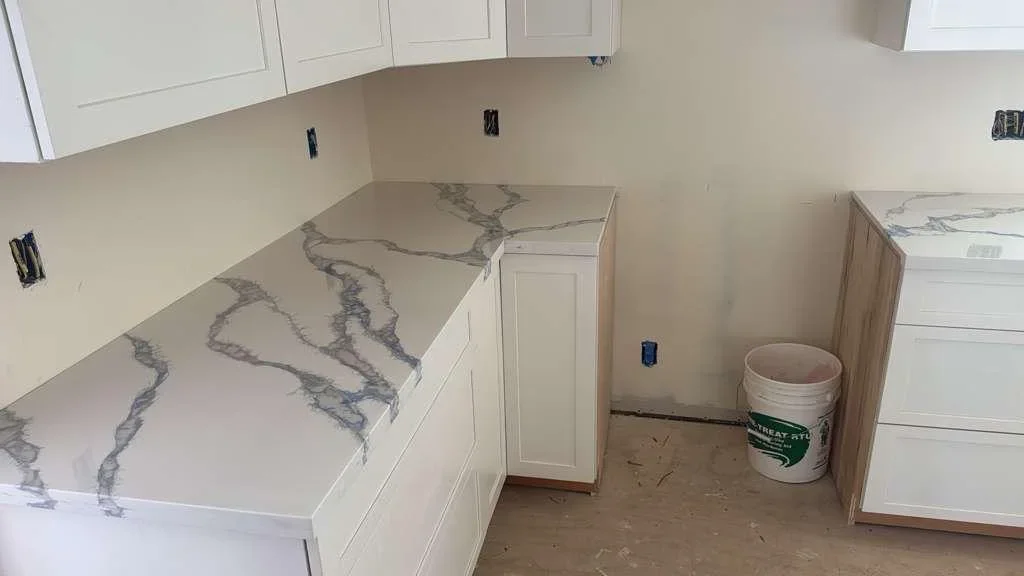 L-shaped kitchen countertop with marble-pattern engineered stone and white cabinets during installation