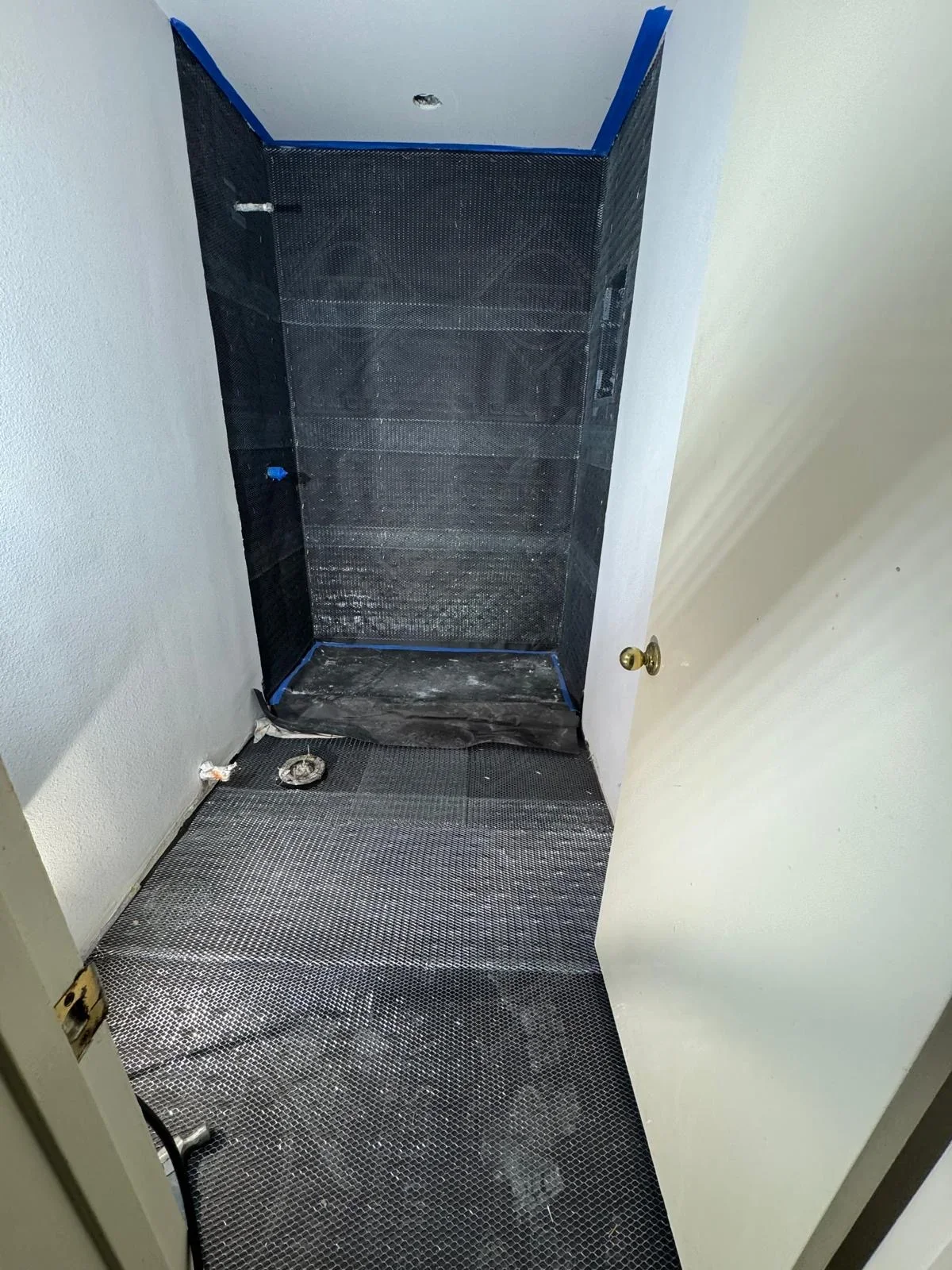 Newly installed shower pan with black textured tile and blue trim edging, showing waterproofing membrane and drainage system