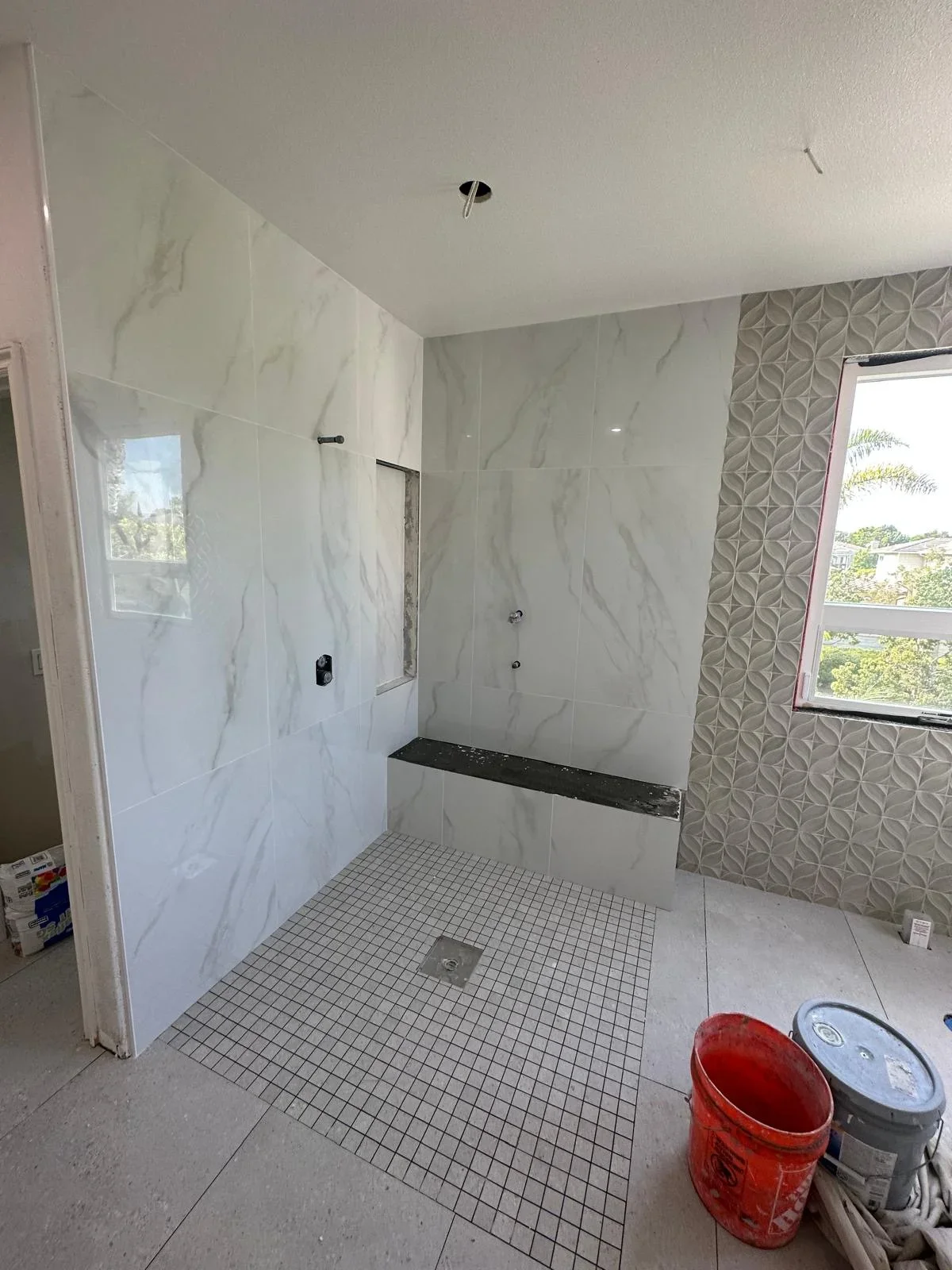 Modern bathroom shower with marble tile walls, black trim, and mosaic floor
