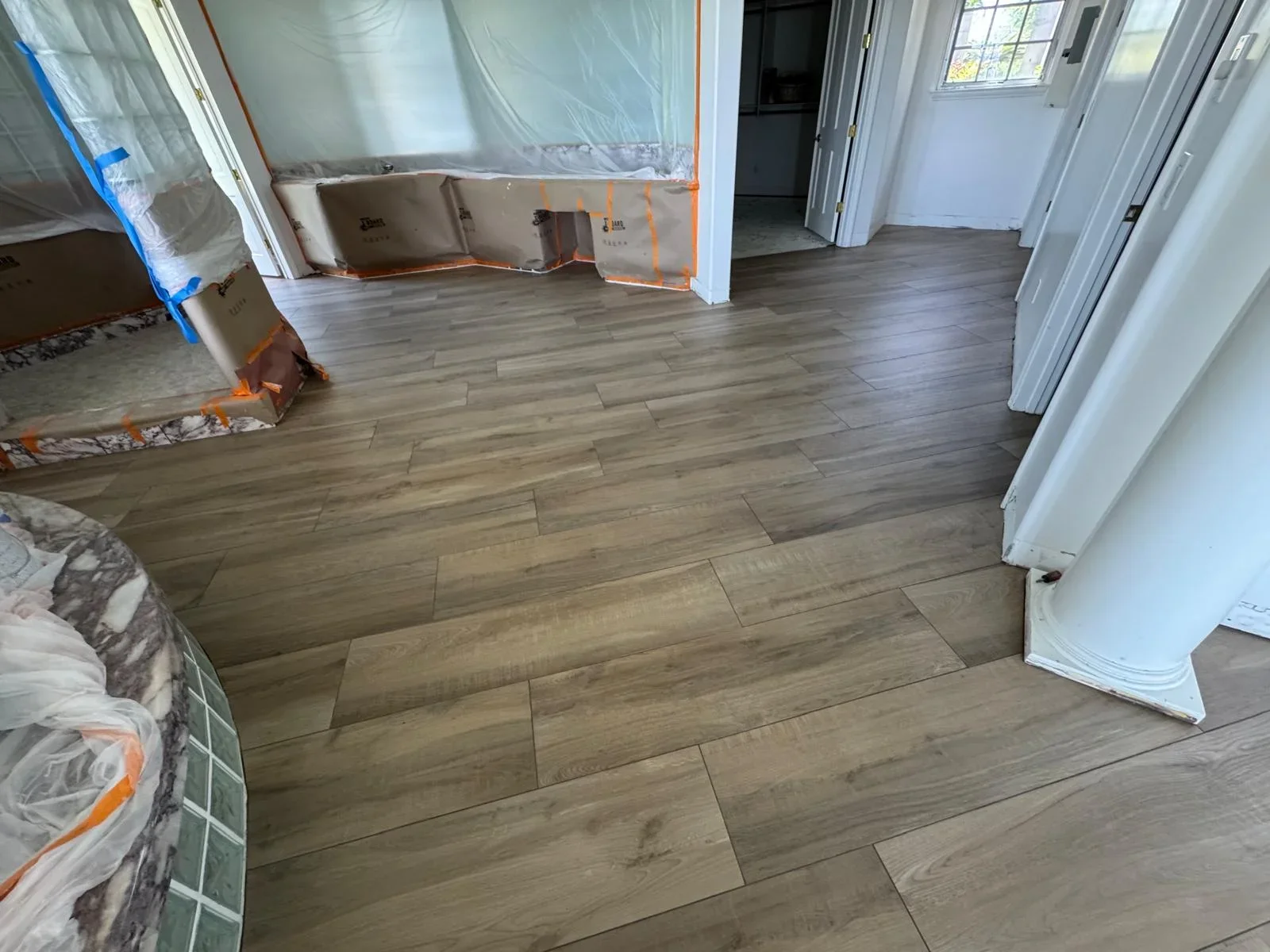 Wood-look vinyl plank flooring installed in open room with white trim and protective plastic sheeting