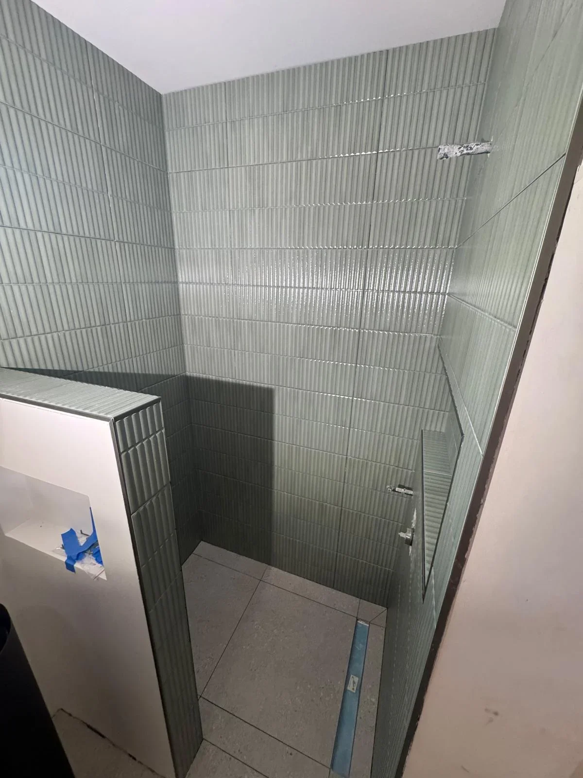 Gray vertical ribbed tile shower enclosure with glass door and tiled floor