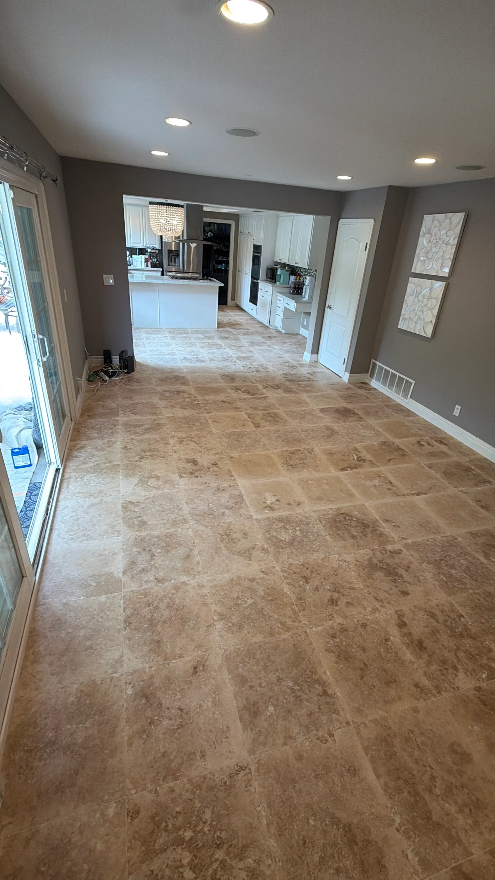Travertine tile flooring in open family room with kitchen visible in background